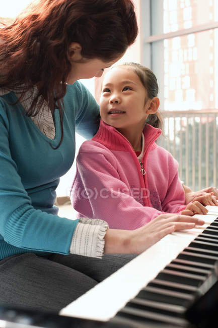 Девочка учится играть на фортепиано с репетитором — стоковое фото