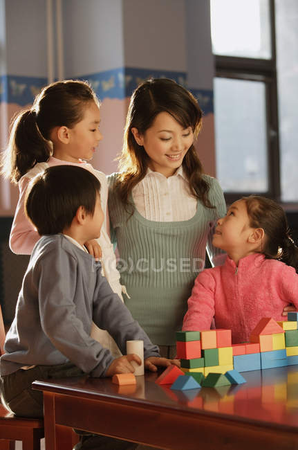 Menino e meninas brincando juntos com o professor — Fotografia de Stock