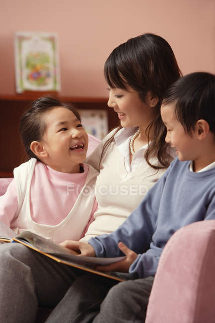Madre con hijo e hija leyendo libro - foto de stock