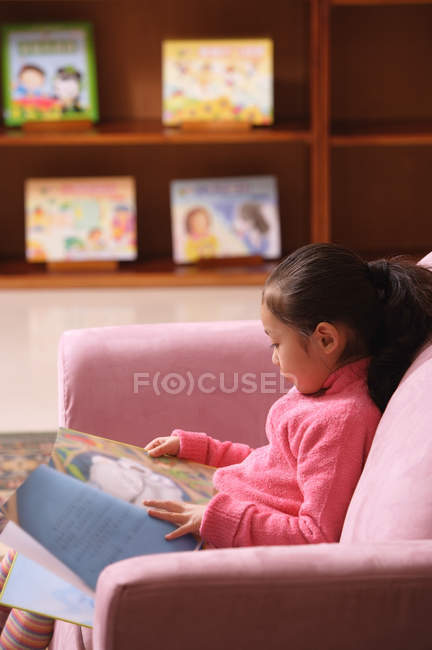 Chica con libro sentado en sofá - foto de stock
