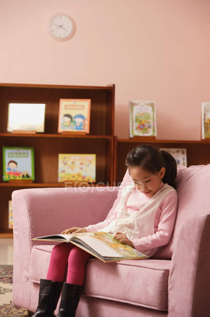 Chica con libro sentado en sofá - foto de stock