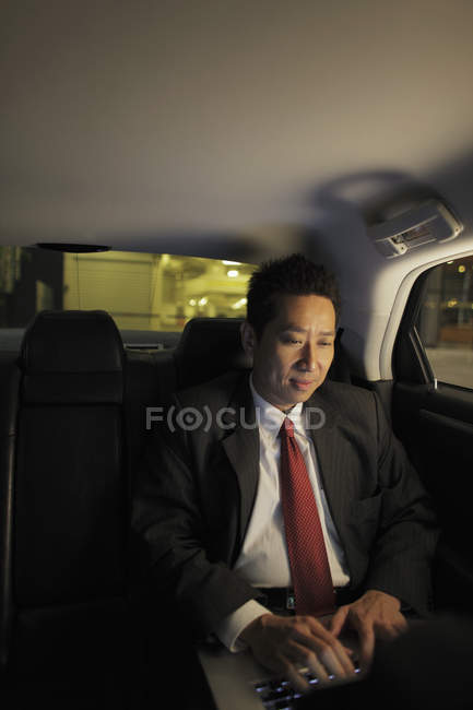 Hombre de negocios sentado en coche y trabajando en el ordenador portátil - foto de stock