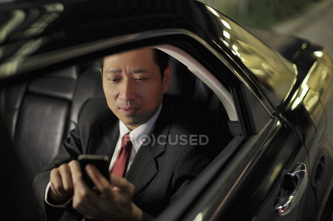 Hombre de negocios sentado en coche y mensajes de texto en el teléfono - foto de stock