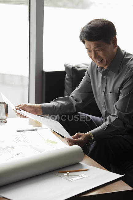 Бизнесмен работает в офисе с чертежами — стоковое фото