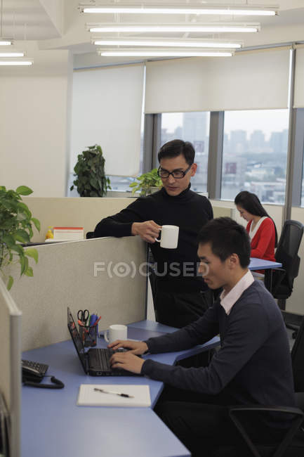 Hombre con taza hablando con su compañero de trabajo - foto de stock