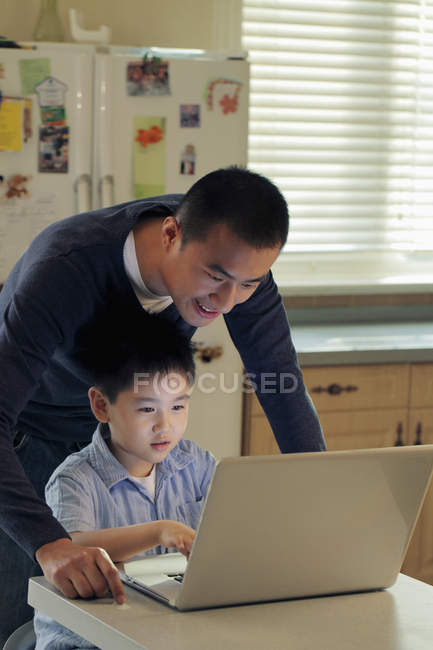 Padre e hijo trabajando en el ordenador portátil - foto de stock