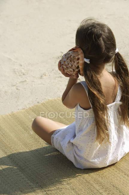 Маленькая девочка слушает ракушку — стоковое фото