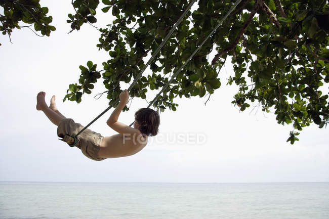 Boy swinging by ocean — Stock Photo