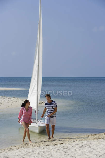 Coppia con barca a vela sulla spiaggia — Foto stock