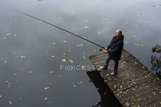 Людина риболовля на озері з пірсу — стокове фото