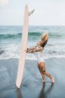 Женщина держит доску для серфинга на пляже — стоковое фото