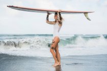 Mujer sosteniendo tabla de surf en la playa - foto de stock