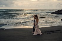 Young couple waling on sandy beach and holding hands at sunset — Stock Photo