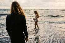 Вид сзади на молодого человека, смотрящего на женщину, идущую по береговой линии — стоковое фото