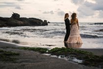 Visão traseira do casal sensual aproveitando o tempo na praia remota ao pôr do sol — Fotografia de Stock