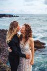 Vista lateral do jovem casal amoroso gentilmente abraçando enquanto está de pé sobre rochas à beira-mar — Fotografia de Stock