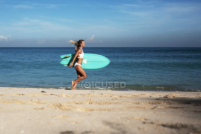 Woman with surfing board running on beach — Stock Photo