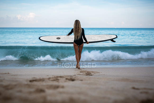 Frau mit Surfbrett steht am Strand — Stockfoto