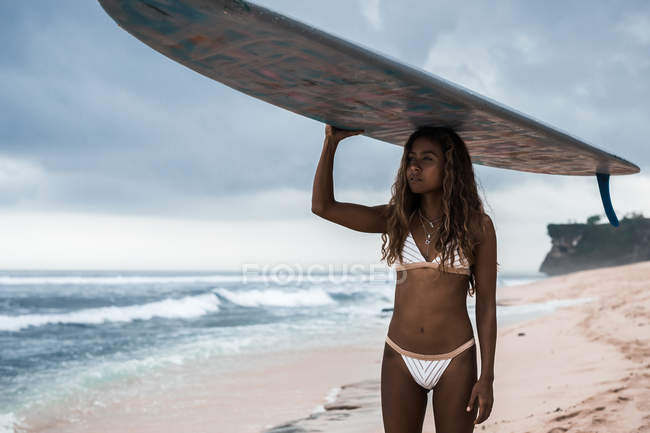 Mujer llevando tabla de surf en la cabeza - foto de stock