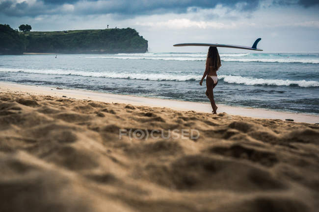 Молода жінка, що носить дошку для серфінгу на пляжі — стокове фото