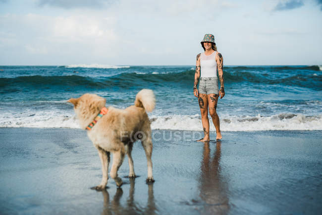 Donna che cammina con cane sulla spiaggia — Foto stock