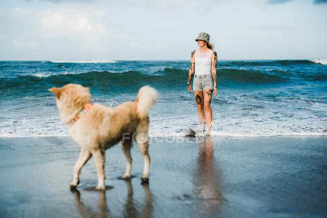 Mulher andando com cão na praia — Fotografia de Stock