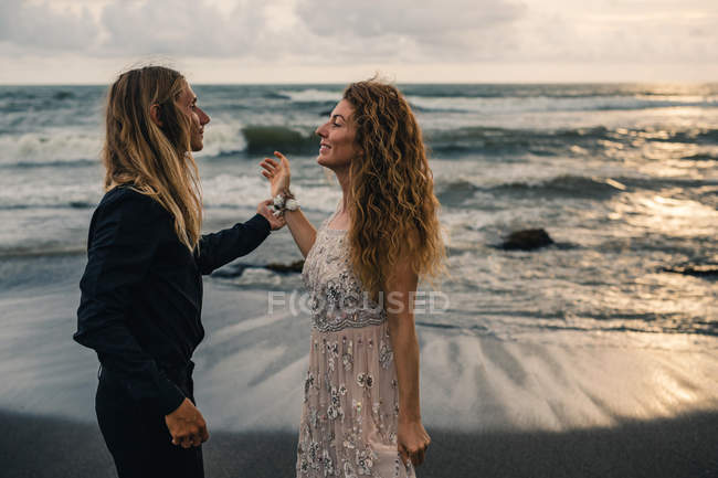 Vista lateral de pareja romántica de pie en la playa de arena al atardecer - foto de stock
