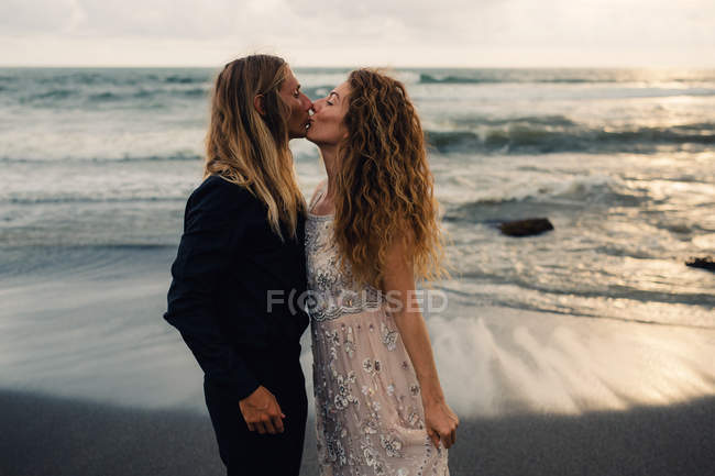 Вид сбоку молодой пары, целующейся на песчаном пляже — стоковое фото