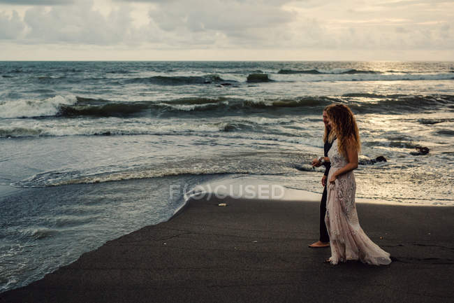 Jeune couple marchant sur une plage de sable fin et se tenant la main au coucher du soleil — Photo de stock
