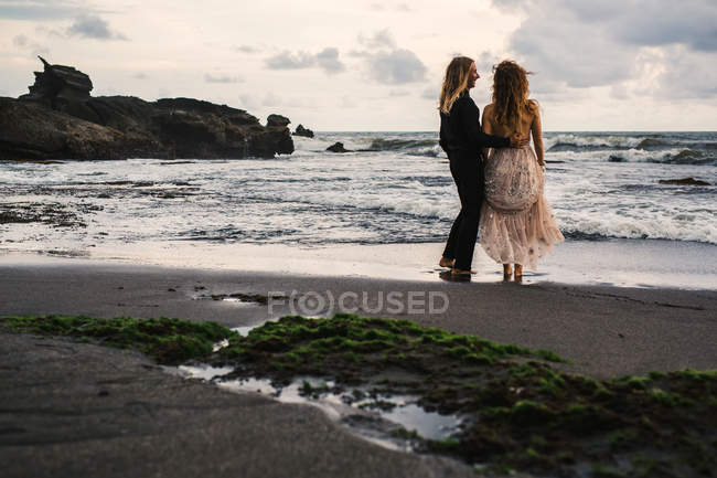 Вид сзади чувственной пары, наслаждающейся временем на отдаленном пляже на закате — стоковое фото