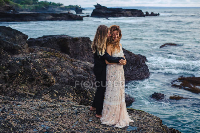 Vista lateral de pareja amorosa abrazándose en rocas junto al mar - foto de stock