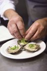 Cropped view of man touching clam with herbs on plate — Stock Photo