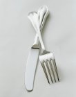 Primo piano vista di forchetta e coltello in metallo incrociato su superficie bianca — Foto stock