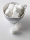 Vista close-up de cubos de açúcar em e ao lado copo branco — Fotografia de Stock