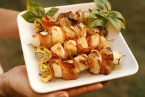 Closeup cropped view of person carrying plate of scallops and bacon skewers — Stock Photo