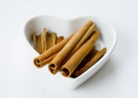 Closeup view of cinnamon sticks in a white heart-shaped bowl — Stock Photo