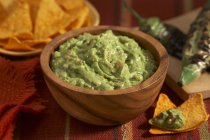 Guacamole in a Wooden Bowl, Tortilla Chips; Charred Jalapeno Peppers — Stock Photo