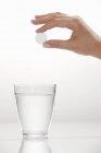 Una mano che tiene una compressa effervescente sopra un bicchiere d'acqua — Foto stock