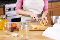 Nahaufnahme abgeschnittene Ansicht einer Frau, die Pfirsiche in Küche schneidet — Stockfoto