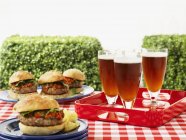 Vista de cerca de hamburguesas y cerveza en una mesa de picnic - foto de stock