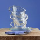 Vue rapprochée des tasses et soucoupes en verre empilées sur serviette pliée et bois — Photo de stock