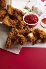 Elevated view of fried chicken wings on paper with dipping sauces — Stock Photo