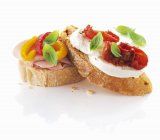 Slices of ciabatta bread with ham, pepper, mozzarella and tomatoes over white background — Stock Photo