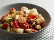 Tomato and pepper salad with croutons on black plate — Stock Photo