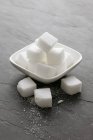 Vista close-up de cubos de açúcar em uma tigela e em uma superfície de xisto — Fotografia de Stock