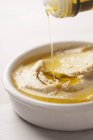 Olive oil being pored over hummus in white bowl — Stock Photo