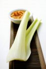 Celery and dip on wooden desk over white background — Stock Photo