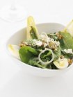 Uma salada verde com nozes, cebolas e molho em prato branco — Fotografia de Stock