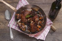 Elevated view of Coq au vin in a copper pan on a wooden surface — Stock Photo