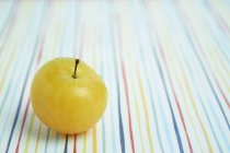 Yellow plum on coloured tablecloth — Stock Photo